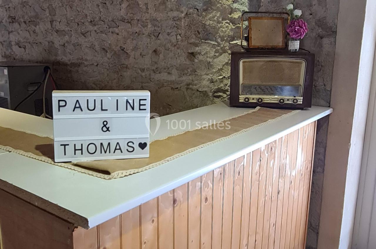 Comptoir en bois avec une boîte lumineuse affichant ’Pauline & Thomas’, une radio vintage et un vase de fleurs.
