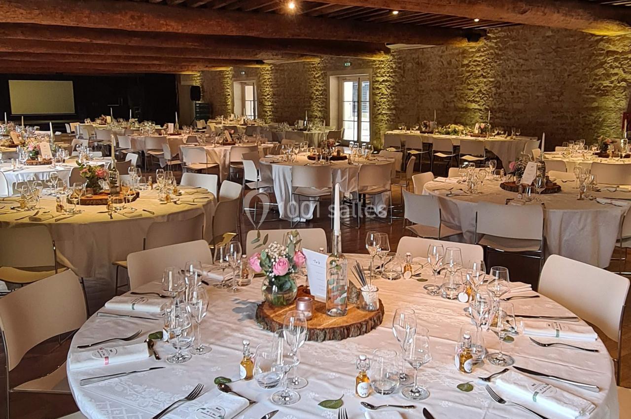 Salle de réception avec tables rondes élégamment dressées, nappes blanches et décoration florale.