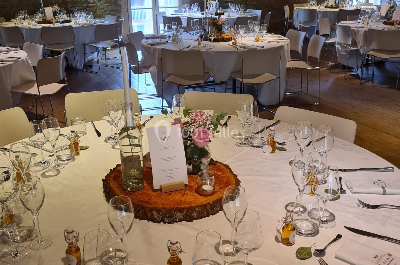 Salle de réception avec tables rondes décorées pour un événement, nappes blanches et centre de table floral.