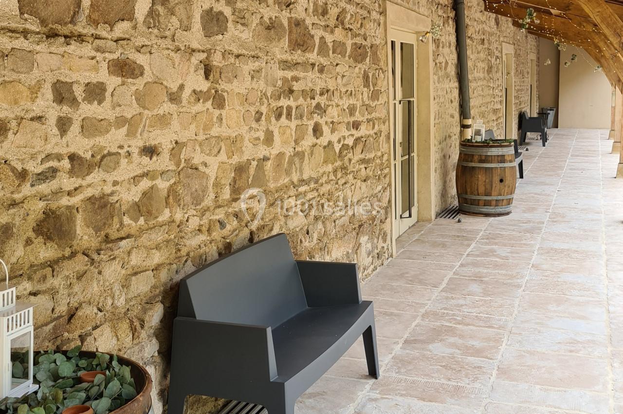 Banc noir et tonneaux décoratifs le long d'un mur en pierre sous un auvent en bois.