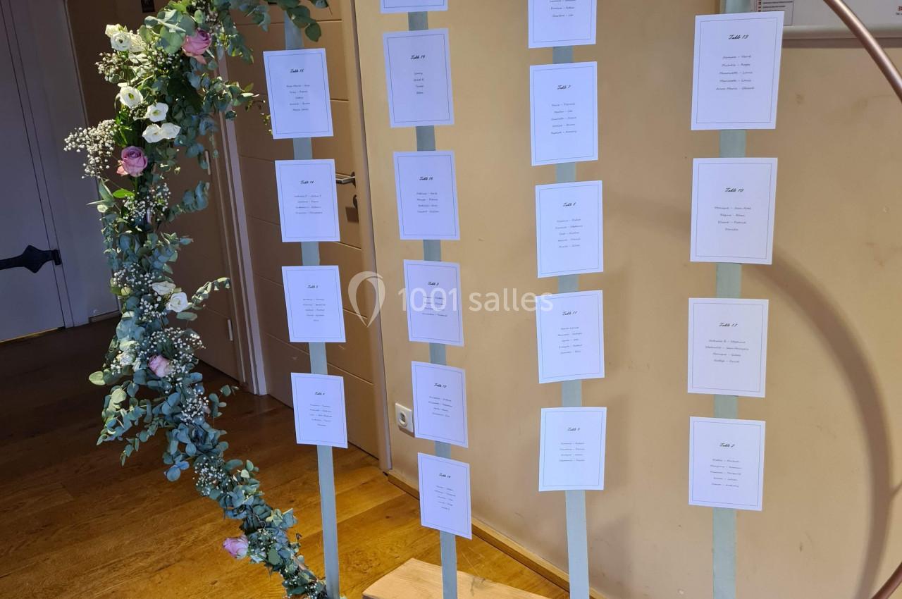 Cercle décoratif en métal avec fleurs et rubans, supportant des cartes de placement pour un événement.