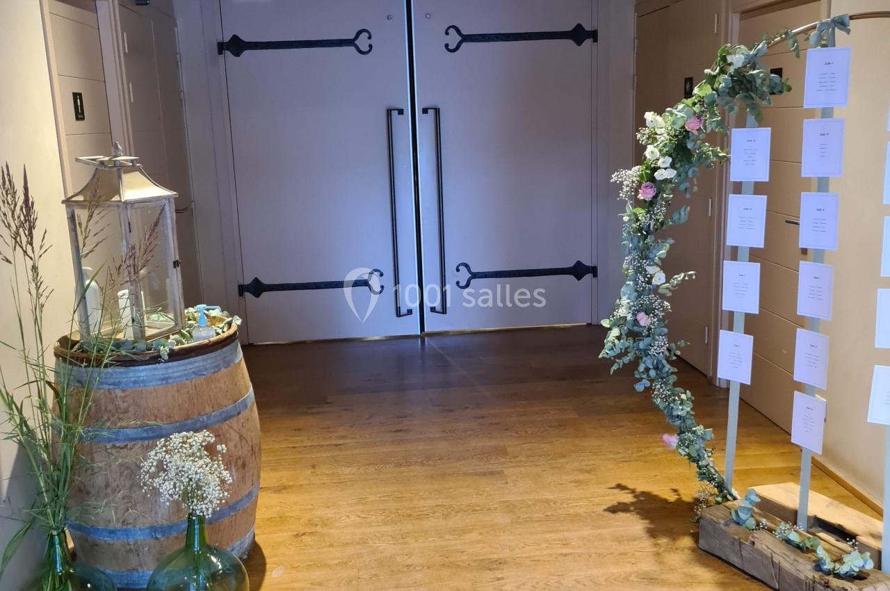 Entrée décorée avec des fleurs, un tonneau avec des vases et un panneau de plan de table, dans un intérieur en bois.