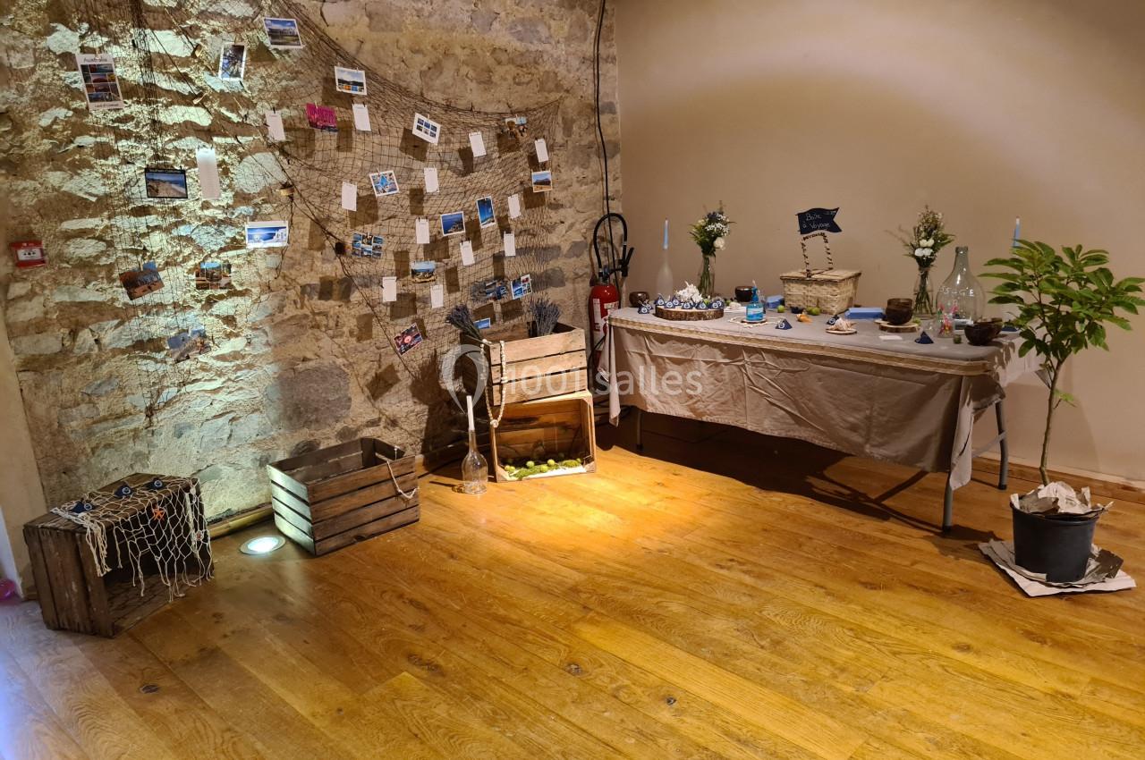 Décoration intérieure avec table ornée d'objets marins, caisses en bois, filet et mur en pierre avec photos suspendues.