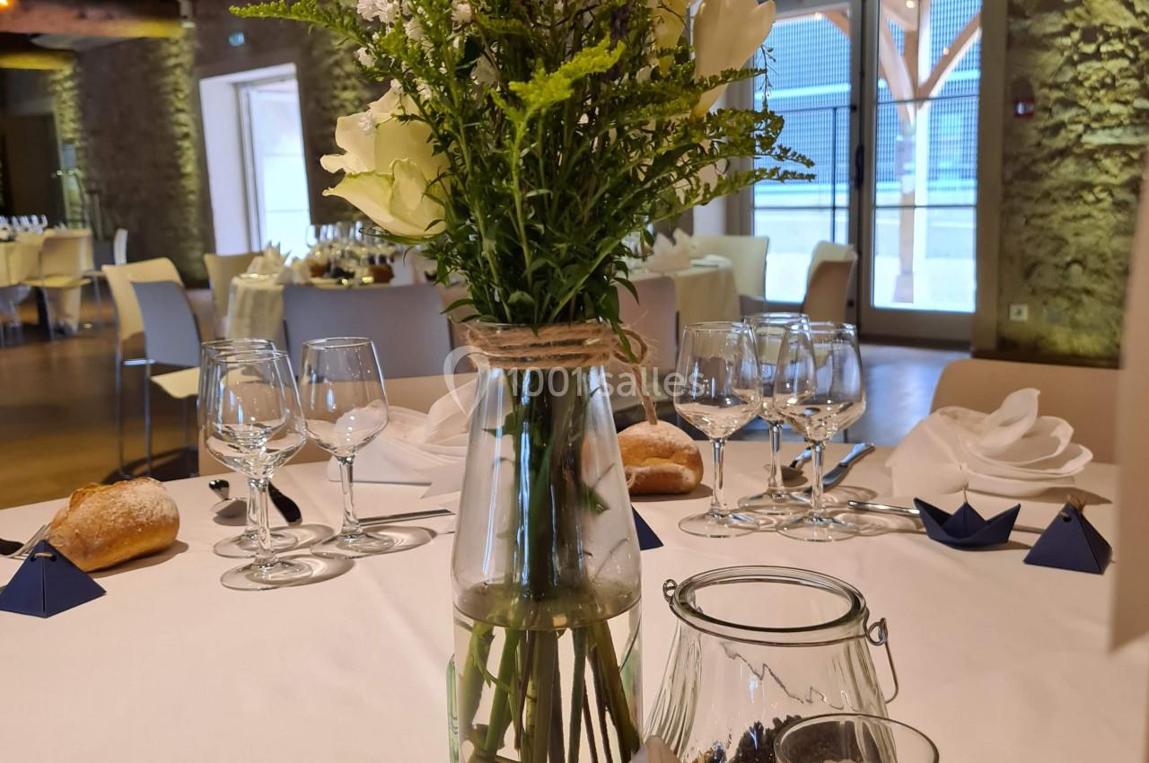 Centre de table avec bouquet champêtre dans un vase en verre, posé sur une rondelle de bois avec menu et bougie.