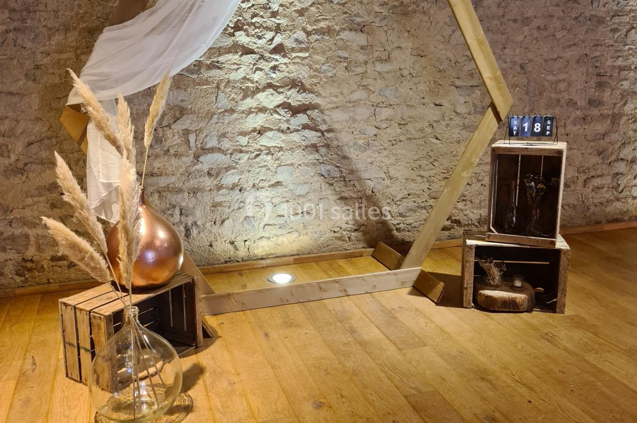 Structure hexagonale en bois décorée d'un voile blanc, entourée de caisses en bois, pampas et objets décoratifs.