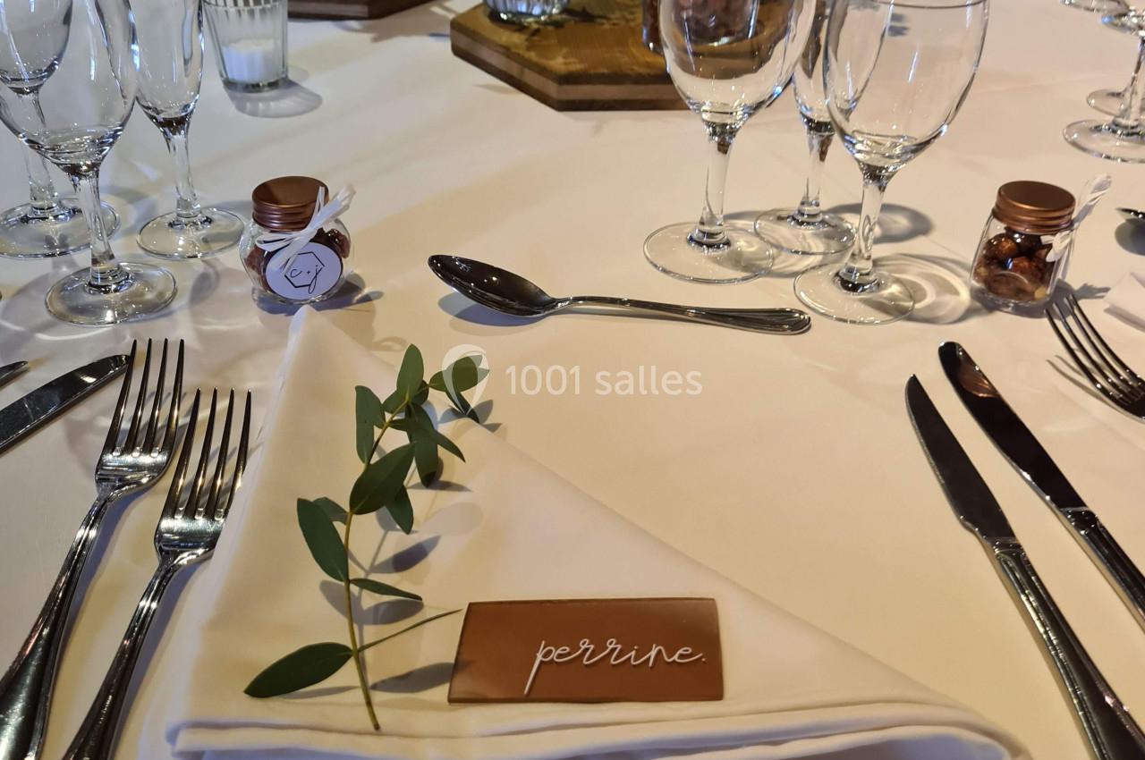 Table dressée pour un repas avec nappe blanche, couverts disposés, marque-place en bois et décoration florale.