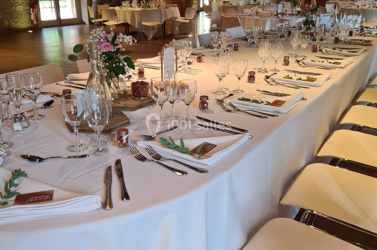 Salle de réception avec longues tables dressées, nappes blanches, vaisselle élégante et décoration florale.