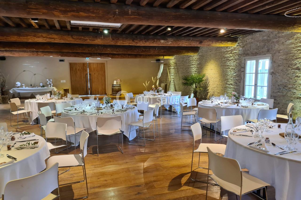 Salle de réception avec tables rondes dressées, chaises blanches et décoration sobre dans un cadre rustique en pierre et…