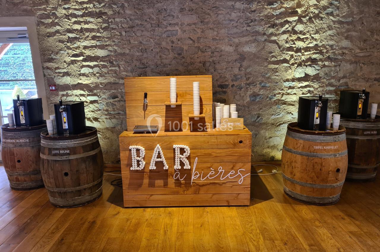 Bar à bières en bois avec tireuses sur des tonneaux, gobelets empilés et mur en pierre en arrière-plan.