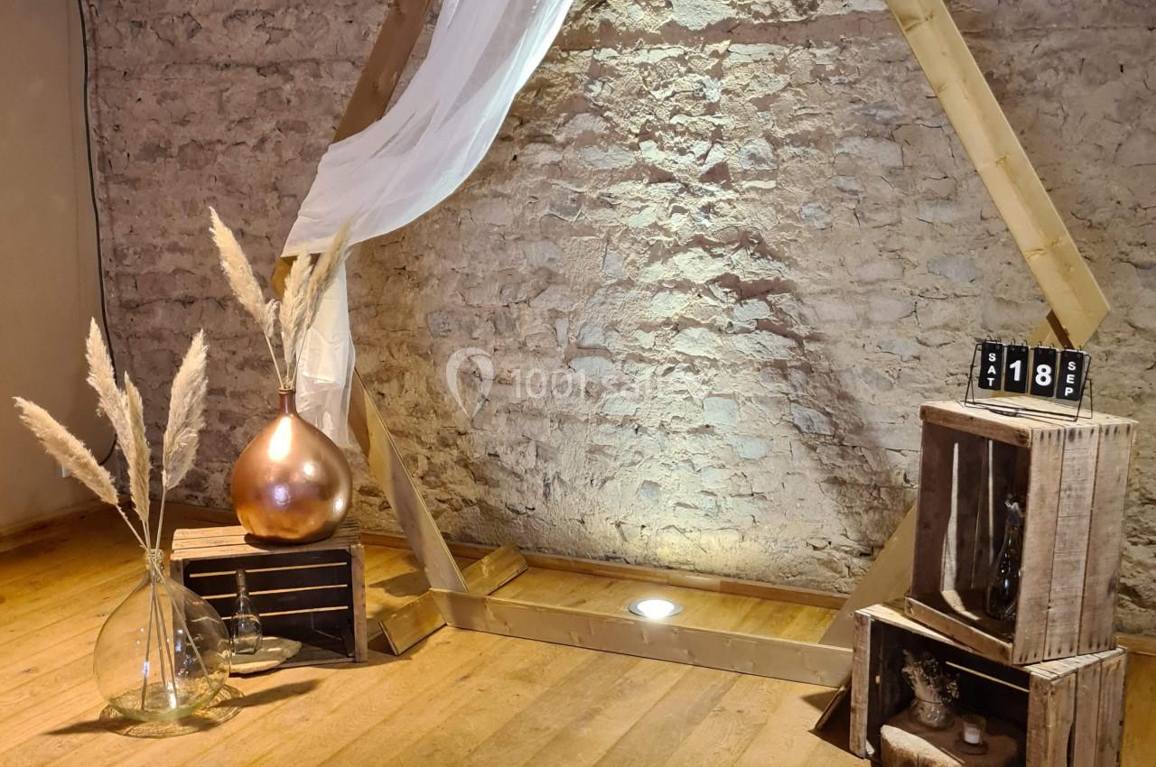 Structure hexagonale en bois décorée de voilage blanc, entourée d'éléments rustiques sur un sol en parquet.