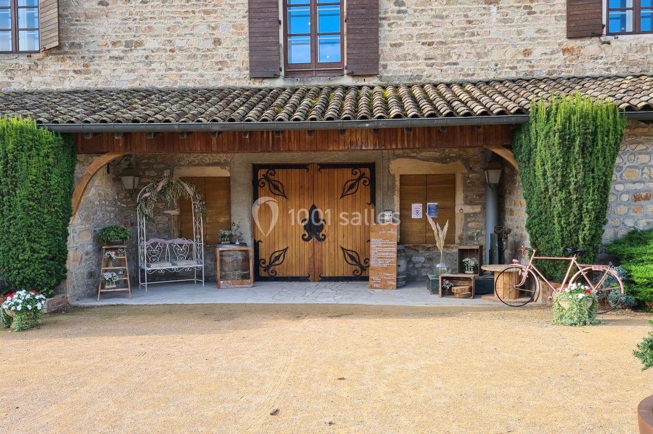 Façade en pierre avec une porte en bois ornée de motifs, entourée de plantes, d'une bicyclette et d'une balançoire…