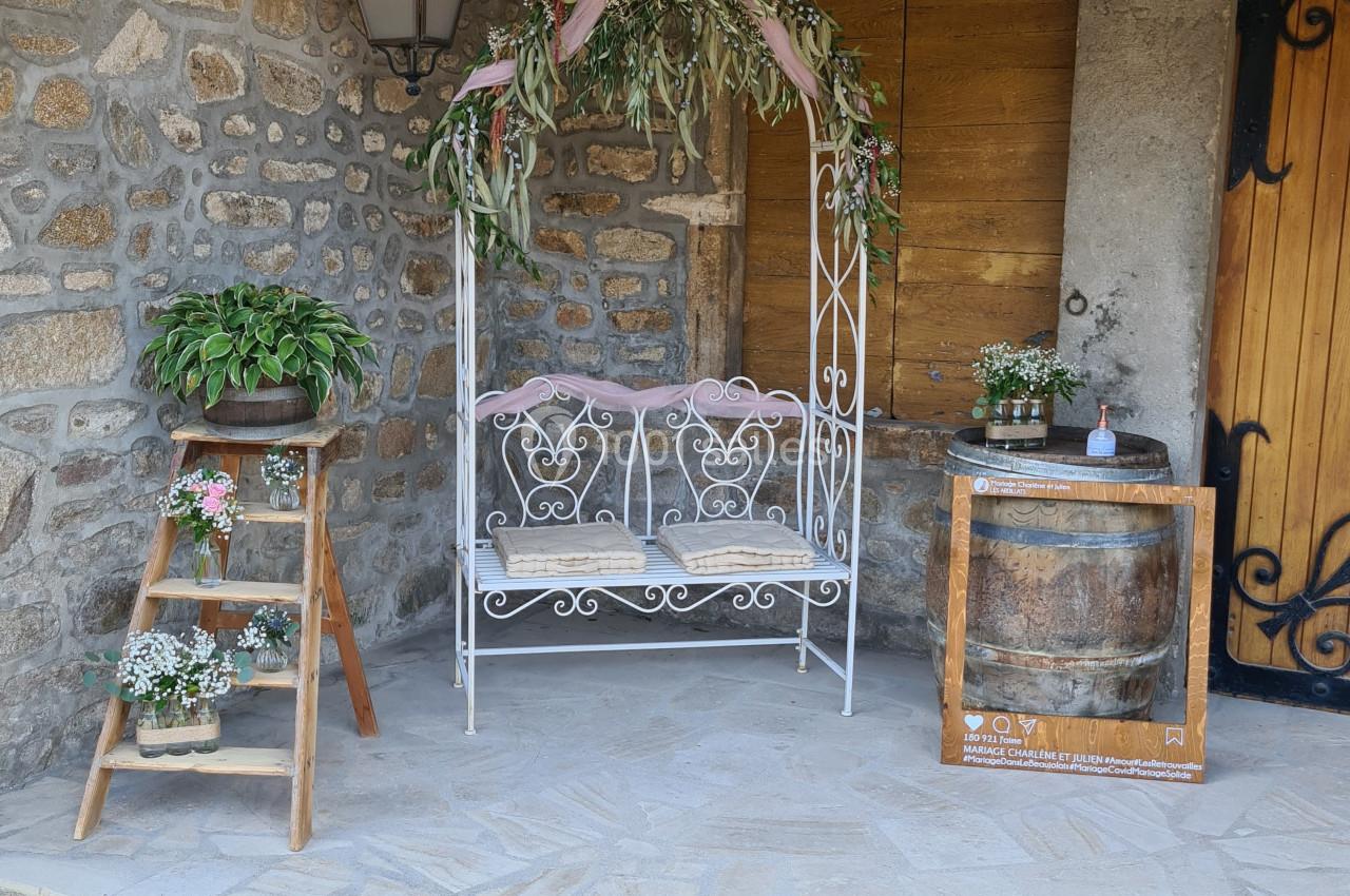 Banc en fer forgé décoré de feuillage, entouré de plantes et d'éléments rustiques sous un porche en pierre.