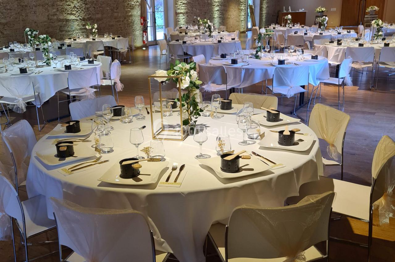 Salle de réception décorée avec des tables rondes dressées, nappes blanches et centres de table fleuris.