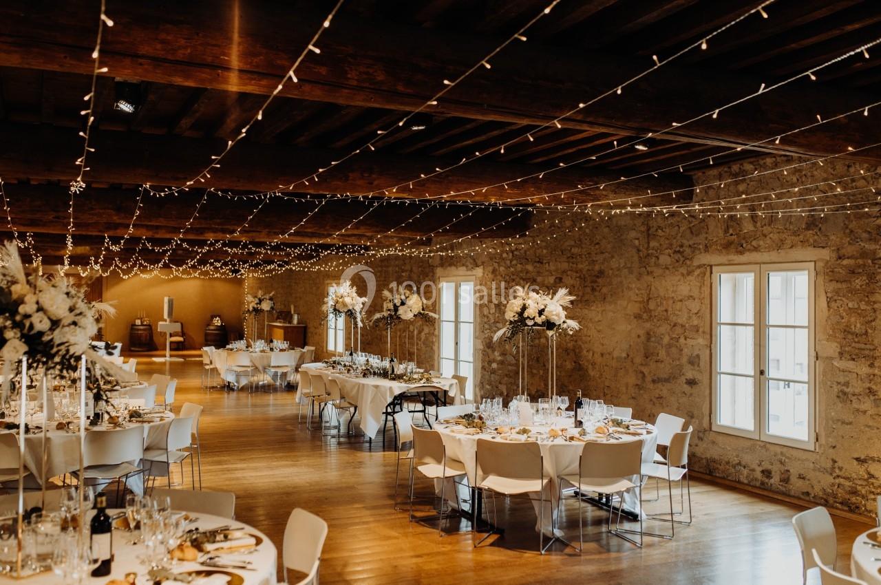 Salle de réception décorée avec des guirlandes lumineuses, des tables dressées et des arrangements floraux élégants.