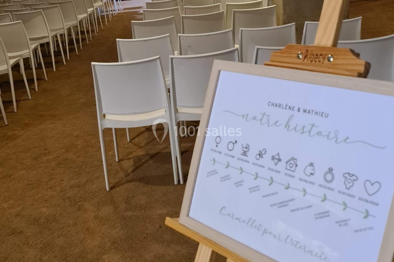 Salle voûtée avec des chaises alignées pour une cérémonie, tableau sur chevalet présentant un programme ou une histoire.