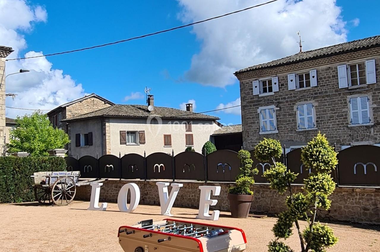 Table de baby-foot sur une place ensoleillée, entourée de pots de plantes, avec des lettres formant ’LOVE’ en arrière-plan.