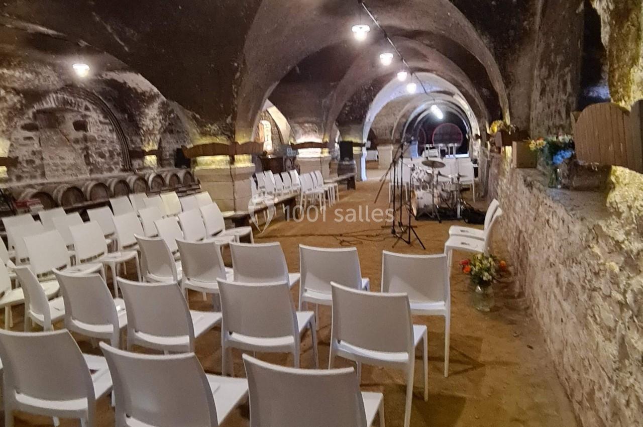 Chaises blanches alignées dans une cave voûtée en pierre, préparées pour un événement ou une cérémonie.