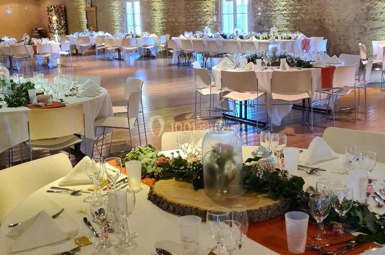 Salle de réception décorée avec des tables rondes dressées, nappes blanches, et centre de table floral.