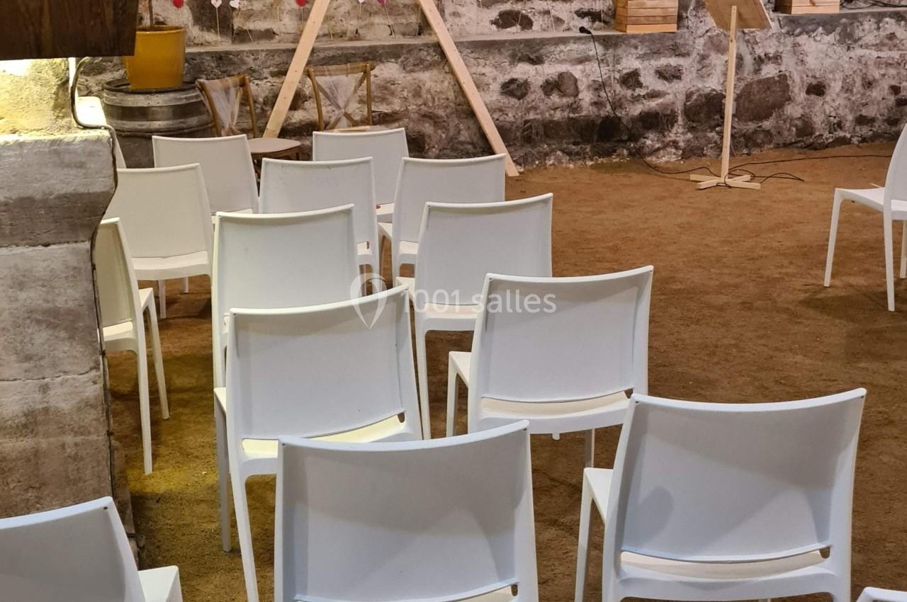 Chaises blanches alignées dans une salle voûtée en pierre avec un présentoir et une structure triangulaire en bois.