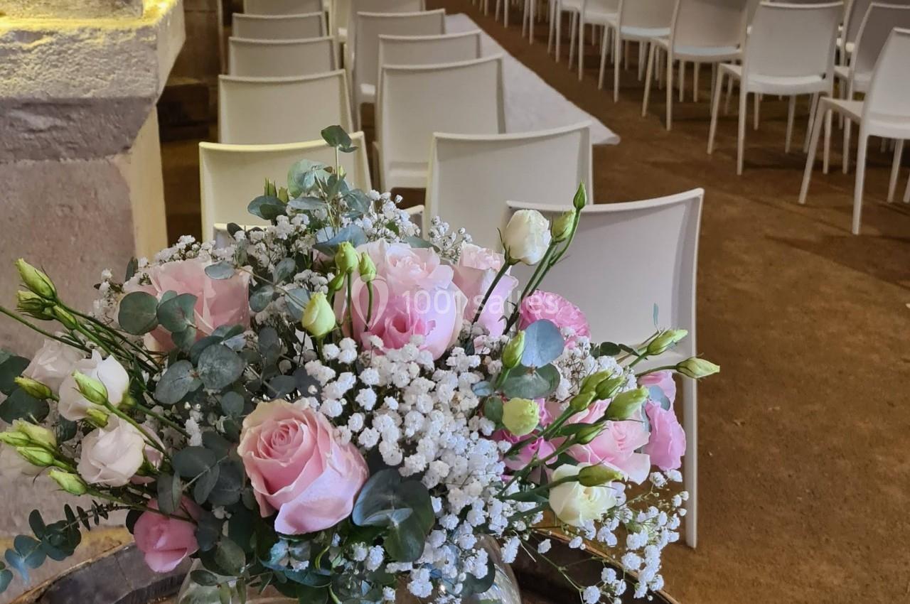 Salle voûtée avec des rangées de chaises blanches, un bouquet de fleurs roses posé sur un tonneau au premier plan.
