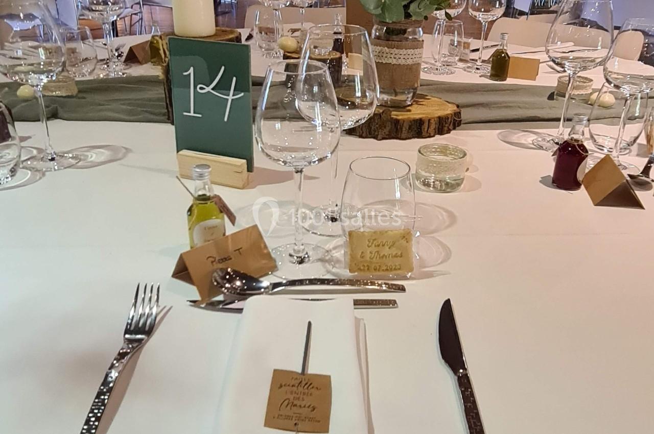 Table dressée pour un repas festif avec couverts, verres, décoration florale et numéro de table dans une salle éclairée.