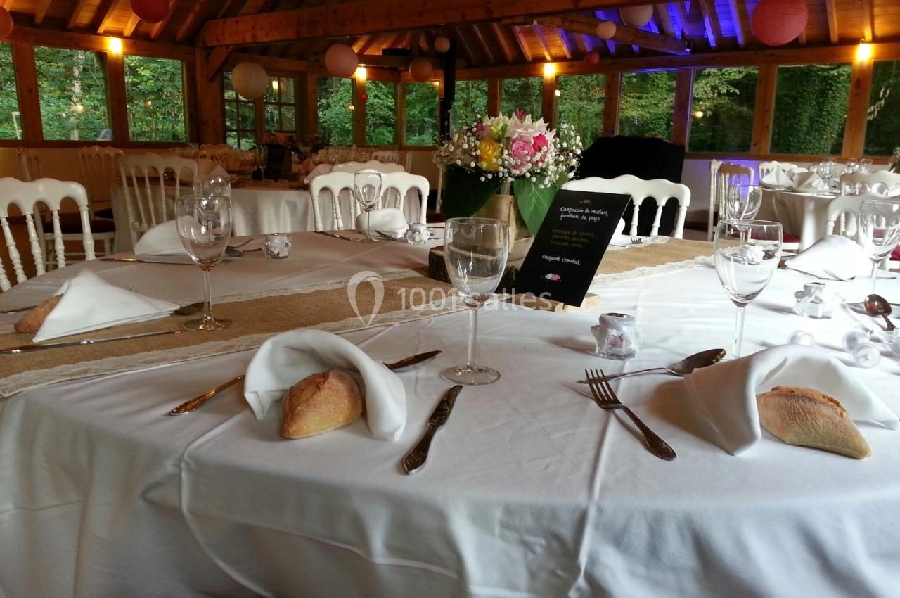 Table dressée pour un repas festif avec nappes blanches, verres, couverts, pain et centre de table floral.
