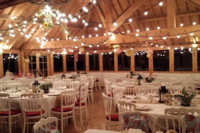 Miniature Location salle Villeneuve-le-Comte (Seine-et-Marne) - Le Domaine de La Pointe #5 Salle de réception décorée avec des guirlandes lumineuses, des tables rondes dressées et un plafond en bois apparent.