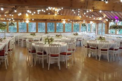 Salle de réception décorée avec des guirlandes lumineuses, des tables rondes dressées et un plafond en bois apparent.