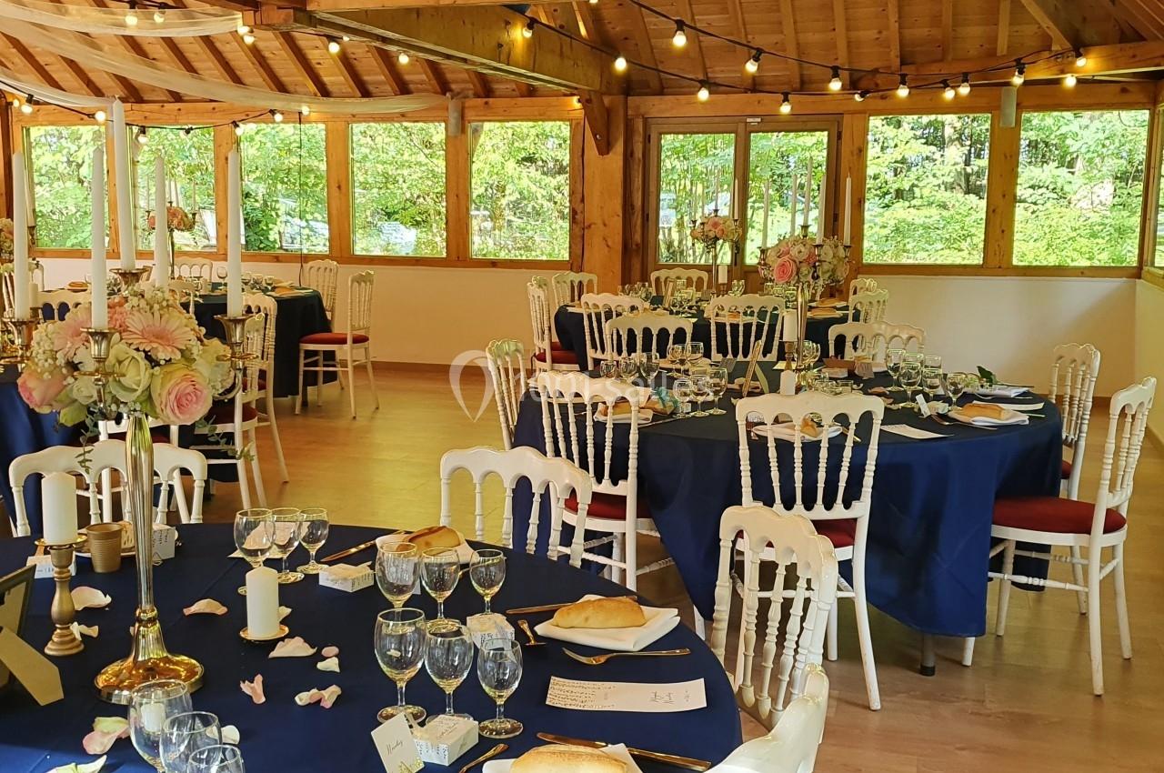 Salle de réception lumineuse avec tables décorées de nappes bleues, bouquets de fleurs et vaisselle élégante.