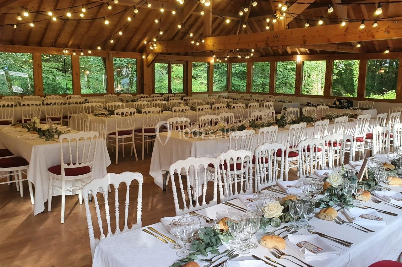 Salle de réception décorée avec des tables dressées, des chaises blanches et des guirlandes lumineuses suspendues.