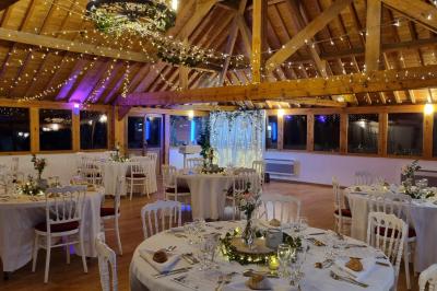 Miniature Location salle Villeneuve-le-Comte (Seine-et-Marne) - Le Domaine de La Pointe #15 Salle de réception décorée avec des guirlandes lumineuses, des tables rondes dressées et un plafond en bois apparent.