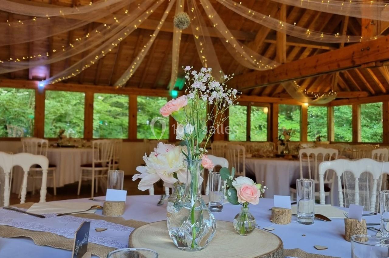 Salle de réception en bois décorée avec des guirlandes lumineuses, des fleurs et des tables dressées pour un événement.