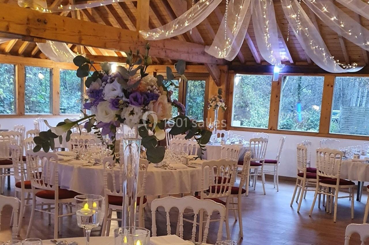 Salle de réception décorée avec des tables rondes, des chaises blanches, des guirlandes lumineuses et un bouquet floral au…
