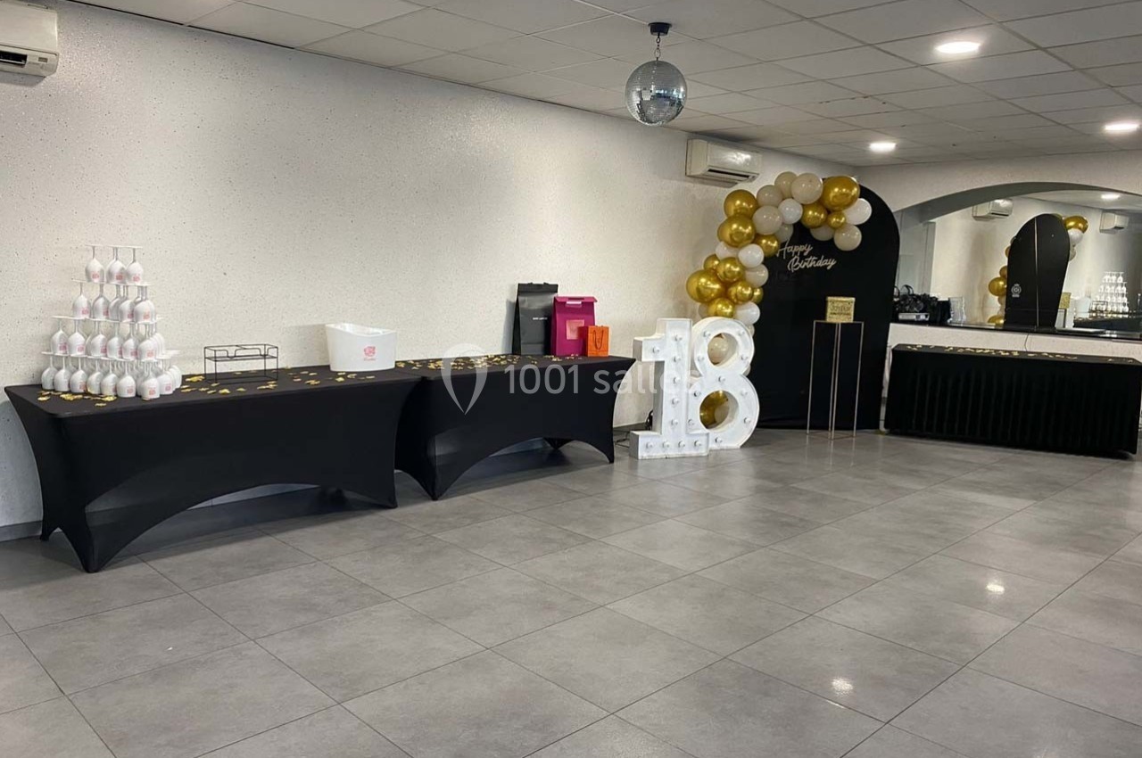 Salle décorée pour un 18e anniversaire avec ballons dorés, tables noires et présentoir à verres.