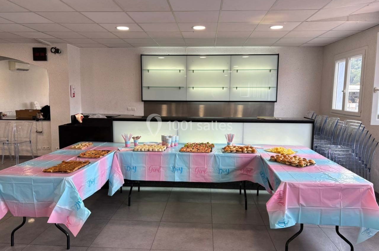 Table garnie de plats variés et décorée de nappes roses et bleues dans une salle lumineuse avec chaises transparentes.