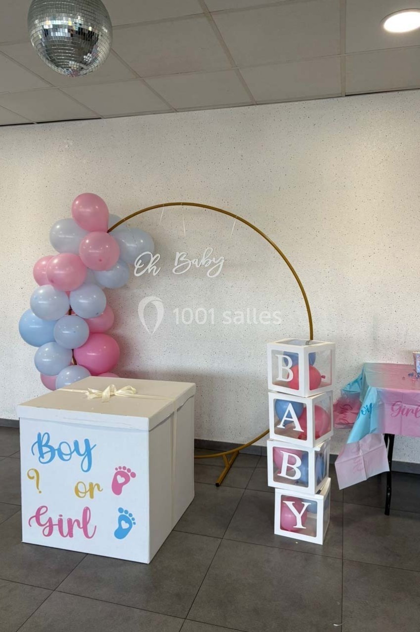Décoration de baby shower avec ballons roses et bleus, cubes ’BABY’, et boîte ’Boy or Girl’ dans une salle.