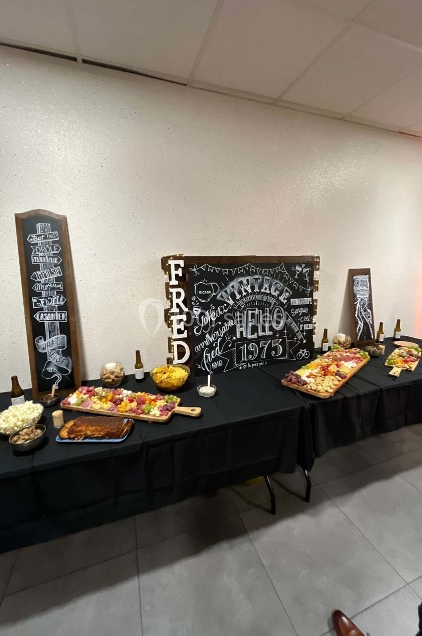 Buffet varié avec planches de charcuterie, apéritifs et décorations murales noires inscrites à la craie.
