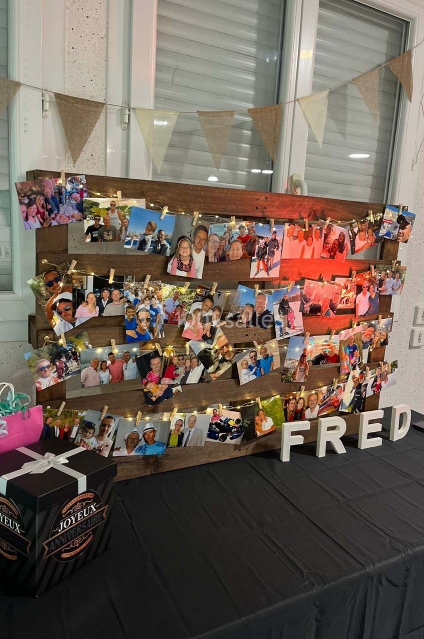 Mur décoratif avec des photos accrochées sur des planches en bois, guirlande lumineuse et lettres formant ’FRED’.