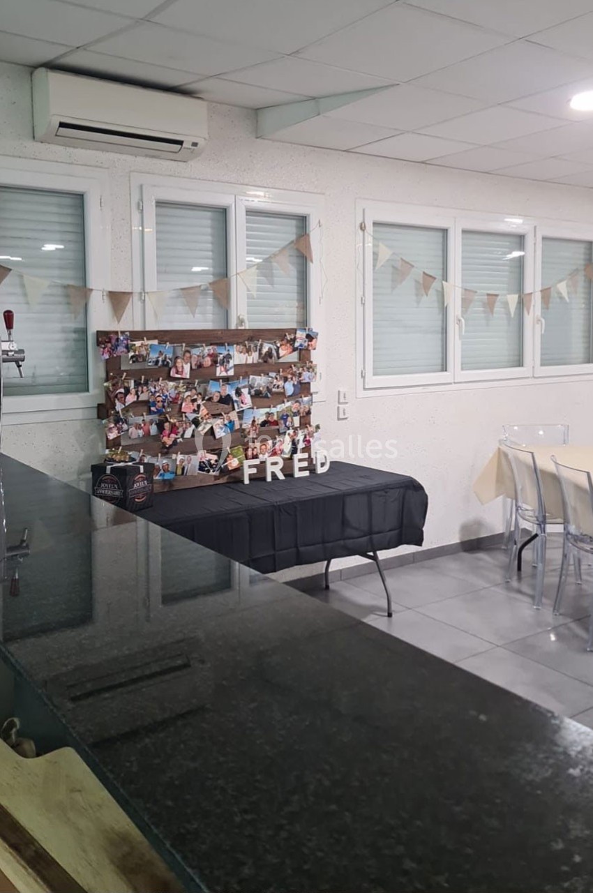 Décoration de salle avec guirlandes, table ornée de photos et lettres ’FRED’, dans un espace lumineux et moderne.