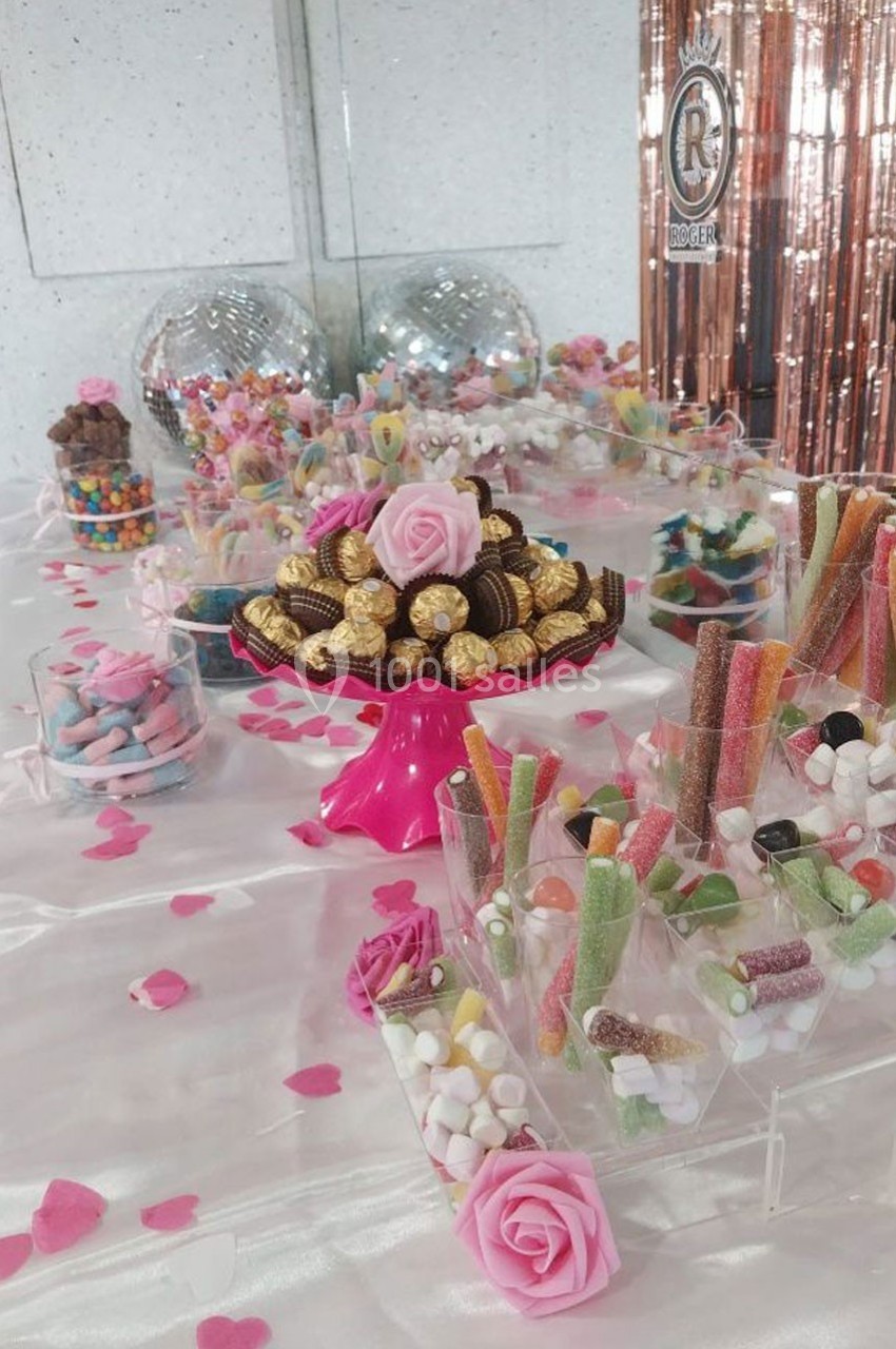 Table décorée avec des bonbons colorés, des chocolats et des roses, entourée de pétales roses et d'éléments festifs.