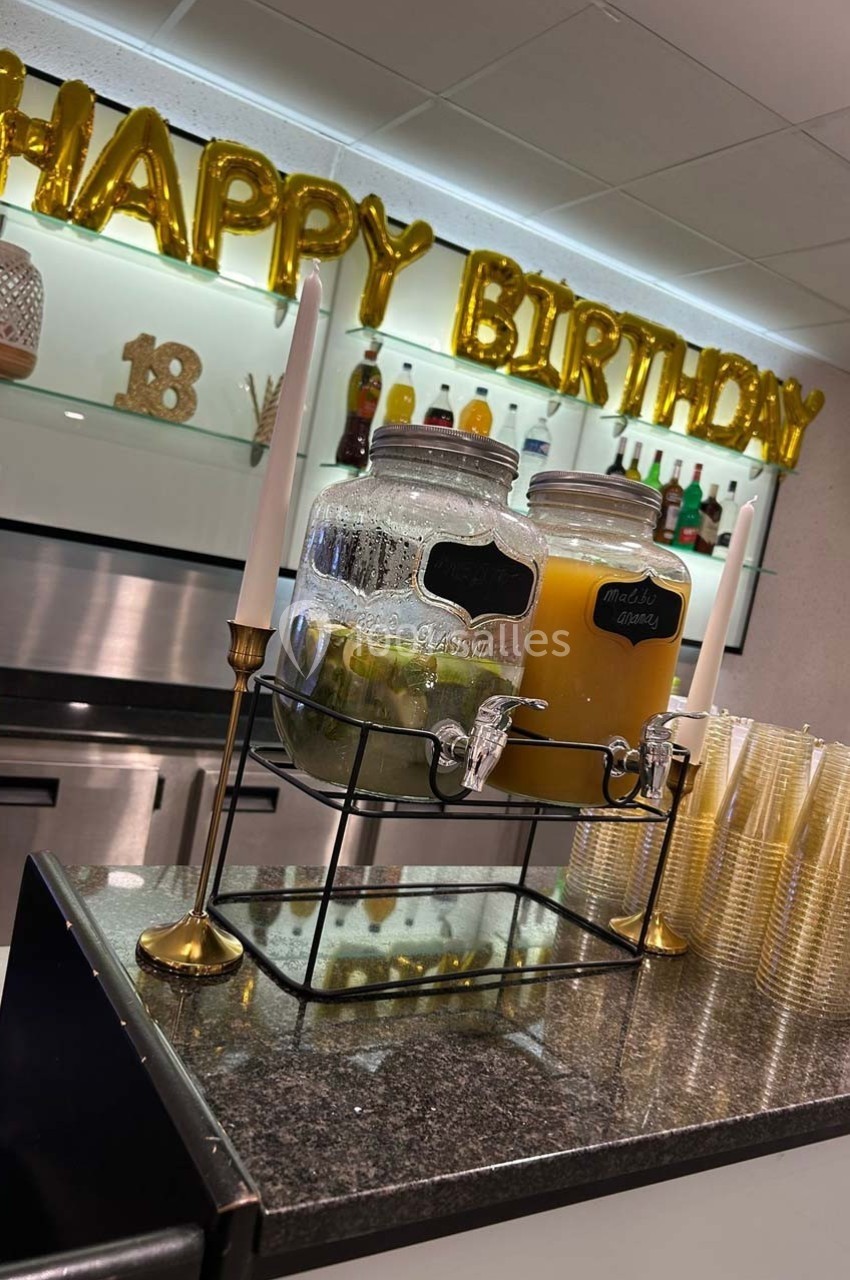 Distributeur de boissons avec jus et eau infusée, posé sur un comptoir, décoré pour un anniversaire.
