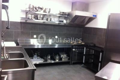 Cuisine professionnelle équipée avec plans de travail en inox, évier double, étagères murales et hotte d'extraction.