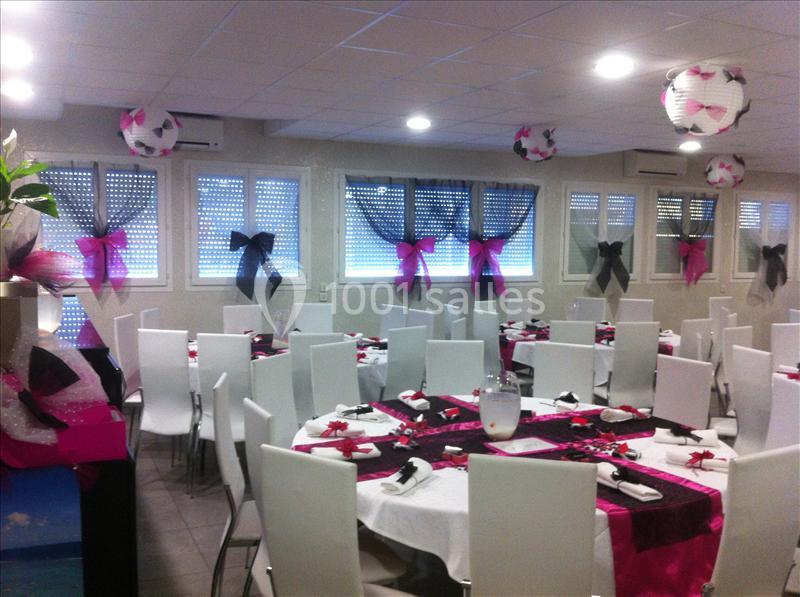 Salle de réception décorée avec des nappes roses et noires, chaises blanches et lanternes suspendues en forme de ballons.