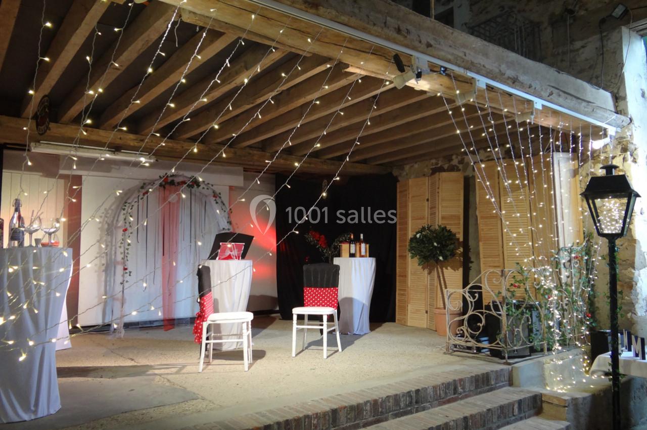 Décoration lumineuse avec guirlandes suspendues dans un espace couvert, comprenant des chaises et des tables décorées.