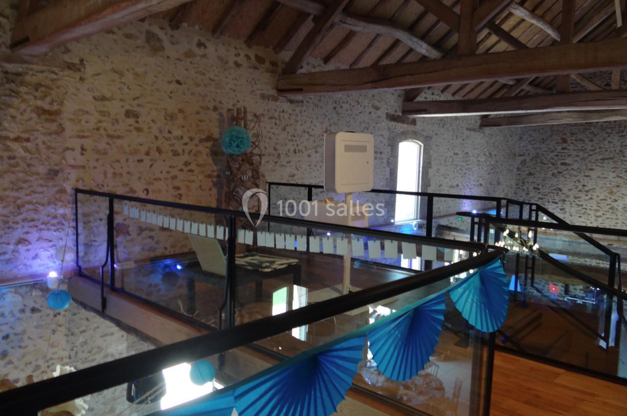 Mezzanine avec sol en verre, rambardes en métal et décoration bleue dans un intérieur en pierre apparente.