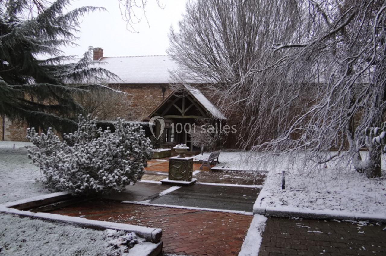Jardin enneigé avec allées en briques, arbres givrés et bâtiment en pierre au fond.
