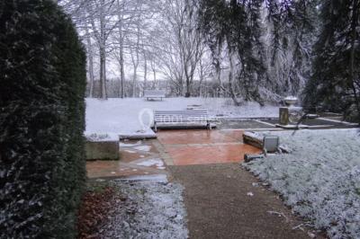 Lit simple avec couvre-lit fleuri dans une chambre lumineuse, éclairée par une lampe de chevet près d'une fenêtre.