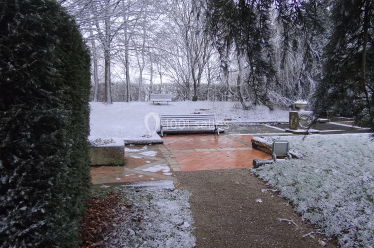 Bancs et allées dans un parc enneigé entouré d'arbres et de végétation givrée.