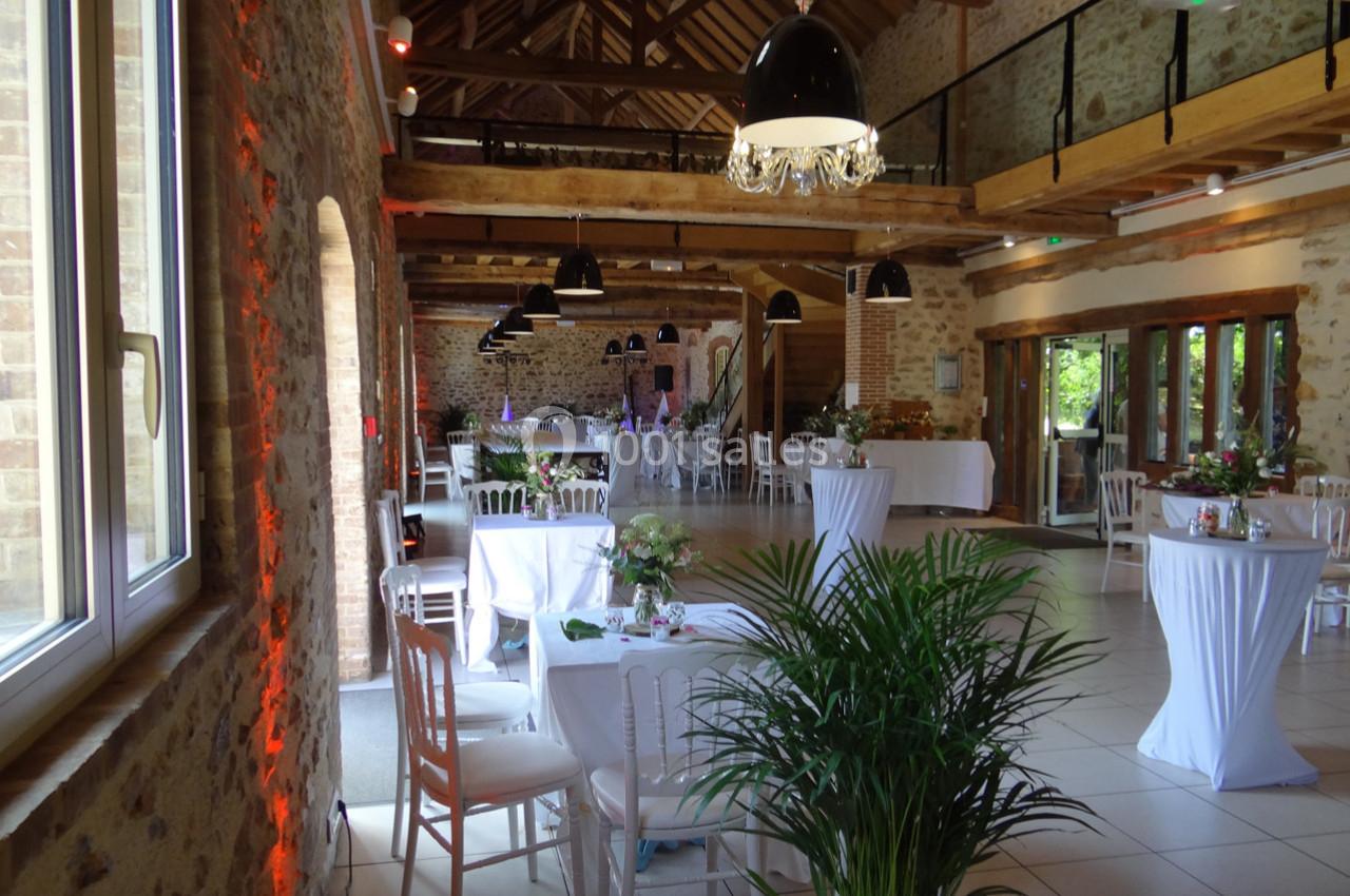 Salle de réception lumineuse avec murs en pierre, poutres apparentes, tables décorées et grandes fenêtres.