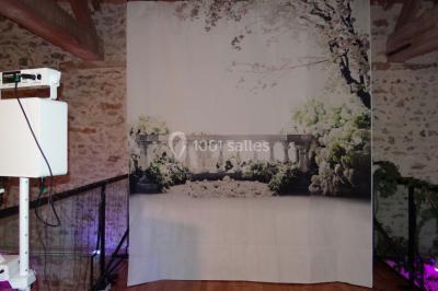 Lit simple avec couvre-lit fleuri dans une chambre lumineuse, éclairée par une lampe de chevet près d'une fenêtre.